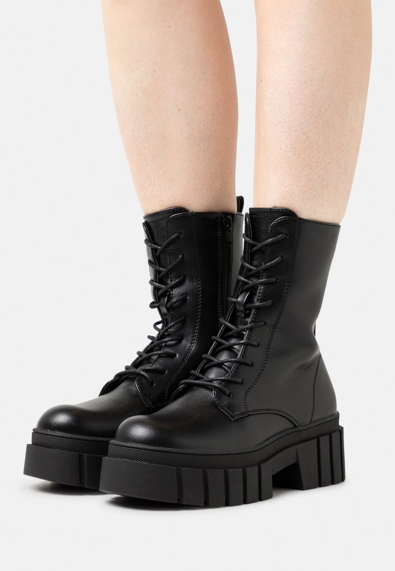 Black leather ankle boots with chunky platform sole, lace-up design, and side zipper for easy wear. Textured upper and reinforced toe.