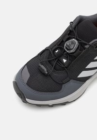 Black and grey athletic shoe featuring a mesh upper, elastic laces, and a textured rubber sole with three white stripes accent.