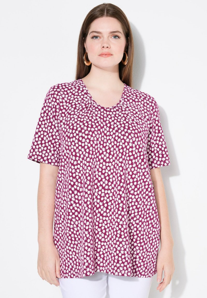 Top de manga corta en tela morada con estampado de margaritas blancas, escote en forma de barco y detalle plisado para un ajuste relajado.