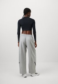 Top corto a maniche lunghe nero con strisce bianche, pantaloni della tuta grigi a gamba larga con spacchi laterali, abbinati a scarpe sportive bianche.