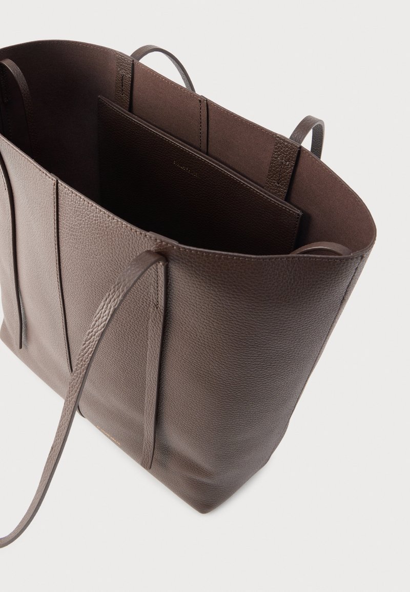 Sac fourre-tout en cuir marron avec surface texturée, ouverture supérieure et deux longues poignées. L'intérieur comprend un compartiment plat séparé.