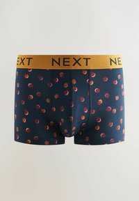 Bóxers azul marino con una cintura amarilla que presenta el logo "NEXT". El diseño incluye llamativos lunares rojos y naranjas con acentos en espiral.