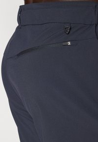 Navy blue trousers with a smooth fabric, featuring a zippered pocket on the right side and a loop detail near the waistband.