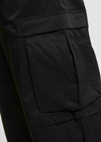 Pantalons cargo noirs avec une grande poche latérale, fabriqués en tissu léger, avec une texture lisse et des détails de couture structurés.