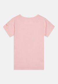 Camiseta de algodón rosa con mangas cortas, escote redondo y un pequeño detalle de logo cerca de la manga izquierda. Textura suave, diseño minimalista.