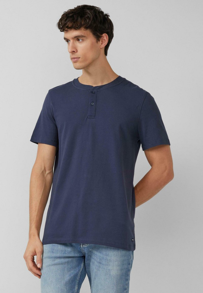 Marineblauw kortermelig henley-shirt van katoen, met een ronde hals, een knoopsluiting met twee knopen en een rechte zoom. Lichtblauwe jeans gedragen.