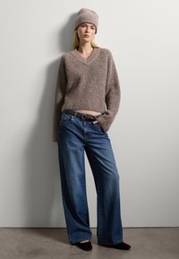 Maglione beige lavorato a maglia con scollo a V, vestibilità oversize e maniche lunghe. Abbinato a jeans blu a gamba larga e un cappello di maglia coordinato.