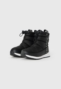 Botas de tornozelo pretas isoladas com tecido texturizado, apresentando uma sola branca e um design de atacadores, acentuadas por uma correia de marcação de lado.