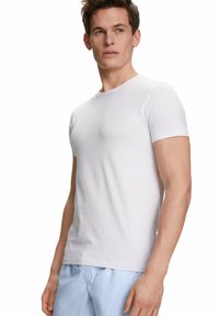 T-shirt blanche à manches courtes avec un col rond, en tissu lisse, design ajusté, associée à un pantalon bleu clair.