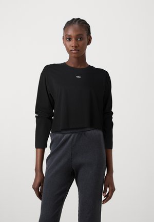Black cropped long-sleeve top with a round neckline and subtle "CPH" logo. Paired with textured dark gray pinstripe pants.