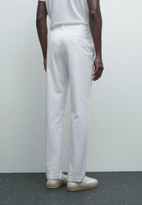 Pantalons en coton blancs à coupe droite, avec des poches latérales et arrière, et une texture lisse et soyeuse. Assortis à des baskets légères.