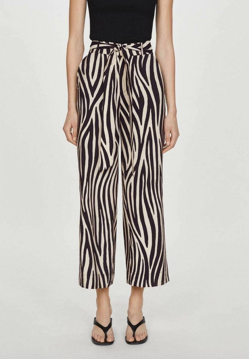 Pantalon à jambes larges à motif zèbre en beige et noir, doté d'une taille nouée, d'un tissu lisse et d'une longueur raccourcie. Accompagné de sandales noires.