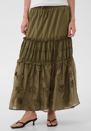 Jupe maxi à volants verte olive avec applications florales texturées, portée avec des sandales noires à talons et un haut blanc, montrée de la taille aux pieds.