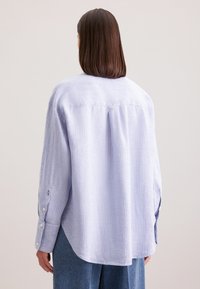 Camicia a maniche lunghe a righe verticali blu e bianche, con una vestibilità rilassata, pieghe posteriori e orlo arrotondato.