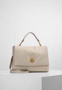 Sac à main en cuir beige avec un logo circulaire en ton doré, une bandoulière ajustable, une finition lisse et une fermeture à rabat.