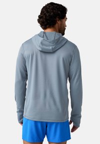 Hellgrau long-sleeve Performance-Hoodie mit strukturiertem Muster und verstellbarem Kapuzen, kombiniert mit blauen Shorts. Mit seitlichen Nähten und Details.