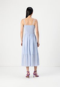 Vaaleansininen, hihaton maksimekko, jossa on smokkityylinen yläosa ja kerroksellinen helma. Yhdistetty violetteihin korkokenkiin.