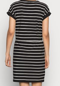 Robe à rayures noires et blanches avec une coupe décontractée, des manches courtes roulées et une taille élastique pour la mise en forme. Tissu doux avec une texture lisse.