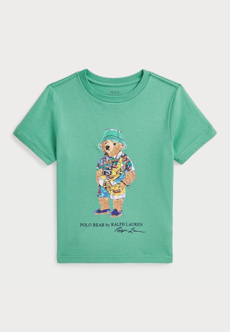 Zaļš kokvilnas T-krekls ar krāsainu ilustrāciju, kurā attēlots lācis cepurē un pludmales apģērba, zem kura ir teksts "Polo Bear by Ralph Lauren".