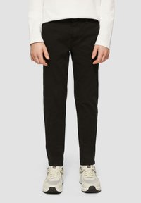 Pantalons noirs ajustés en coton avec une texture lisse. Portés avec des sneakers de couleur claire présentant un design en maille et des accents.
