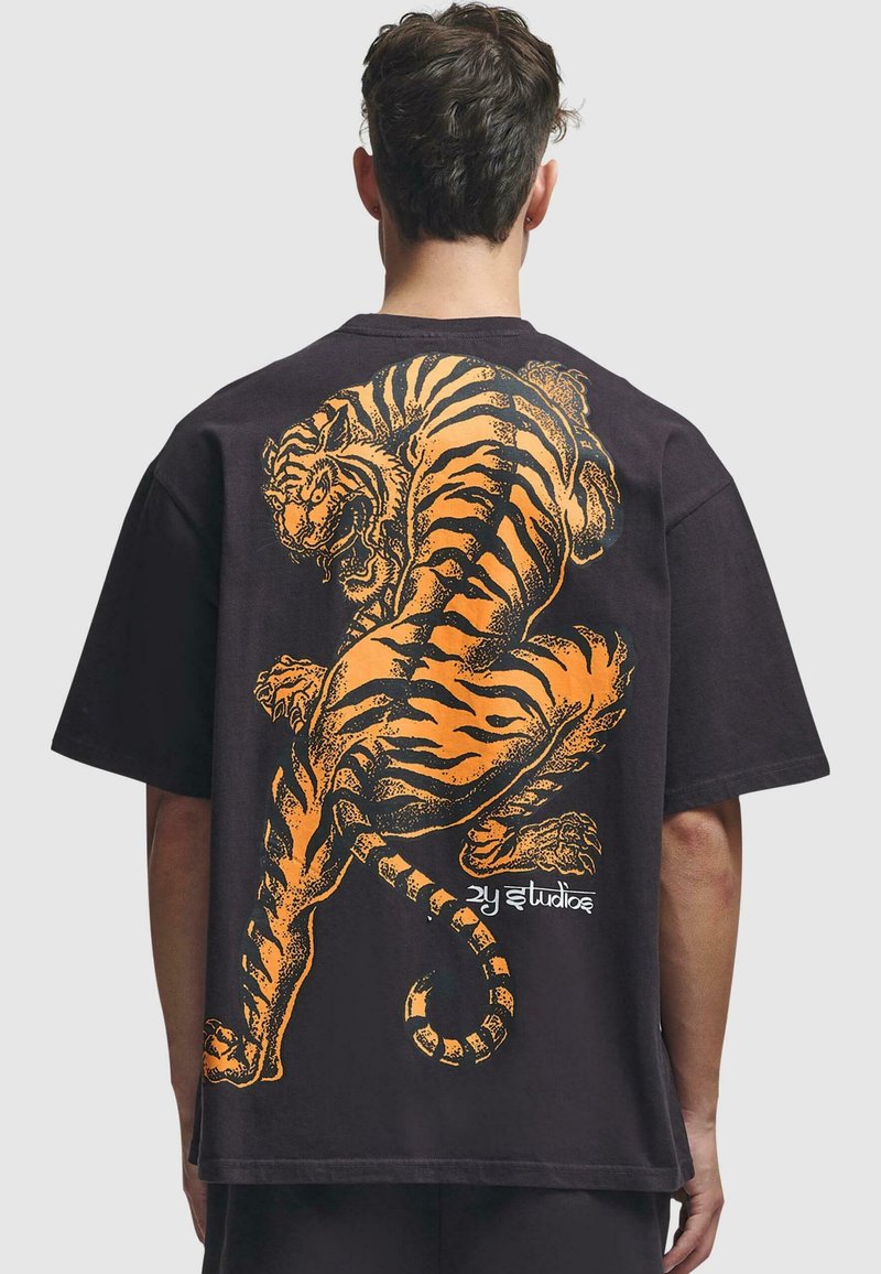 Camiseta oversized negra con un gran gráfico de tigre naranja en la parte posterior, con rayas detalladas y un diseño de cola ondulada.