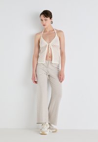 Gehaakte haltertop in crème met een striksluiting aan de voorkant, gecombineerd met beige en witte gestreepte wijde broek. Sneakers maken de outfit af.