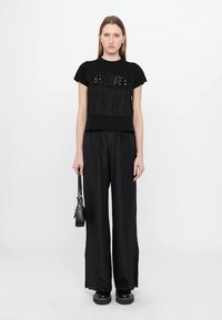 Black cropped t-shirt with fringe detail on the front, paired with black wide-leg pants and chunky black boots. Small black handbag.