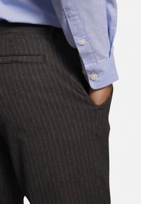 Grijze broek met krijtstrepen van getextureerde stof. Een lichtblauw overhemd met omgeslagen manchetten is gedeeltelijk zichtbaar naast de broek.