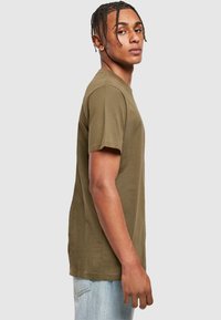 Olive green cotton t-shirt, short sleeves, crew neck, relaxed fit, smooth texture, displayed on a model from the side.