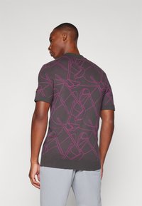 Dark gray short-sleeve polo shirt featuring a vibrant pink abstract pattern, ribbed collar, and a slightly relaxed fit.