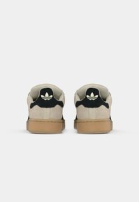 Sneakers with a beige suede upper, black accents, gum rubber sole, and a logo design on the heel. Flat laces and padded collar.
