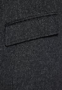 Ciemnoszara wełniana tkanina z ukośnym wzorem w jodełkę. Posiada naszywaną kieszeń z czystym, stębnowanym brzegiem. Teksturowana powierzchnia.