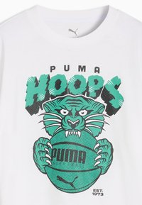 Λευκό μπλουζάκι με τιρκουάζ γραφικό ενός άγριου τίγρη που κρατάει μια μπάλα του μπάσκετ και έντονο κείμενο "PUMA HOOPS" από πάνω, "EST. 1973" από κάτω.