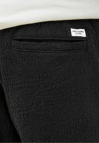 Pantalon en tissu noir texturé avec une petite poche arrière et une étiquette de marque Jack & Jones blanche au-dessus de la poche.