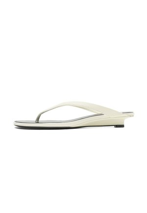 Sandale plate beige avec une fine bride à l'orteil et un talon légèrement surélevé, vue de côté sur fond blanc.