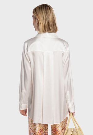 Blouse en satin blanc avec col, manches longues et poignets boutonnés. Dotée d'un pli dans le dos pour plus de détail et d'une texture globalement lisse.