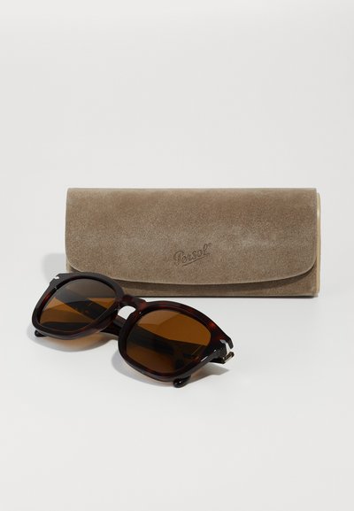 Süveg mintás napszemüveg barna lencsékkel, amelynek merész négyzet alakja van. Esetében egy világos barna velúr védőtok, fedélzáras kialakítással.