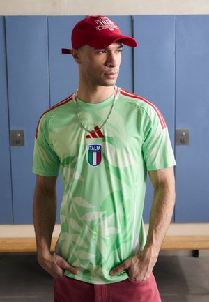 Green athletic jersey with leaf patterns, red Adidas stripes on shoulders, Italia logo in front. Paired with a red cap and silver necklace.