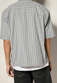 Korte mouwen geruit overhemd in blauw en wit, met een relaxte pasvorm, button-down kraag en een rechte zoom, gedragen over een wit shirt.