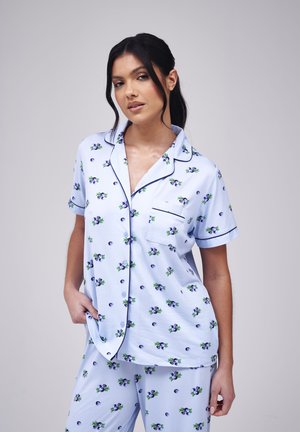 Lyseblåt pyjamasæt med et blomsterprint af lilla blomster og grønne blade. Skjorten har korte ærmer, knapper og en lomme.