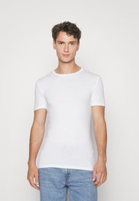 T-shirt bianco a maniche corte realizzato in tessuto morbido, con scollo rotondo e design aderente, abbinato a jeans azzurri chiari.