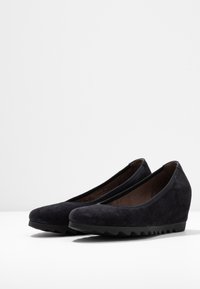 Chaussures à talon compensé en daim noir avec un bout rond, un dessus texturé et un motif en zigzag sur la semelle en caoutchouc. Conception élégante et épurée.