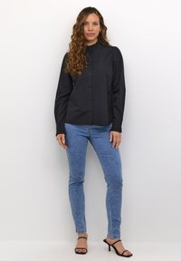 Černá košile na knoflíky s řaseným límcem, spárovaná s světle modrými slim-fit džíny a černými sandály na podpatku. Jednoduchý, čistý design.