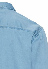 Lichtblauwe denim overhemd met een puntslotkraag, zichtbare stiksels en een zachte textuur. De afbeelding toont de achterzijde van het overhemd.