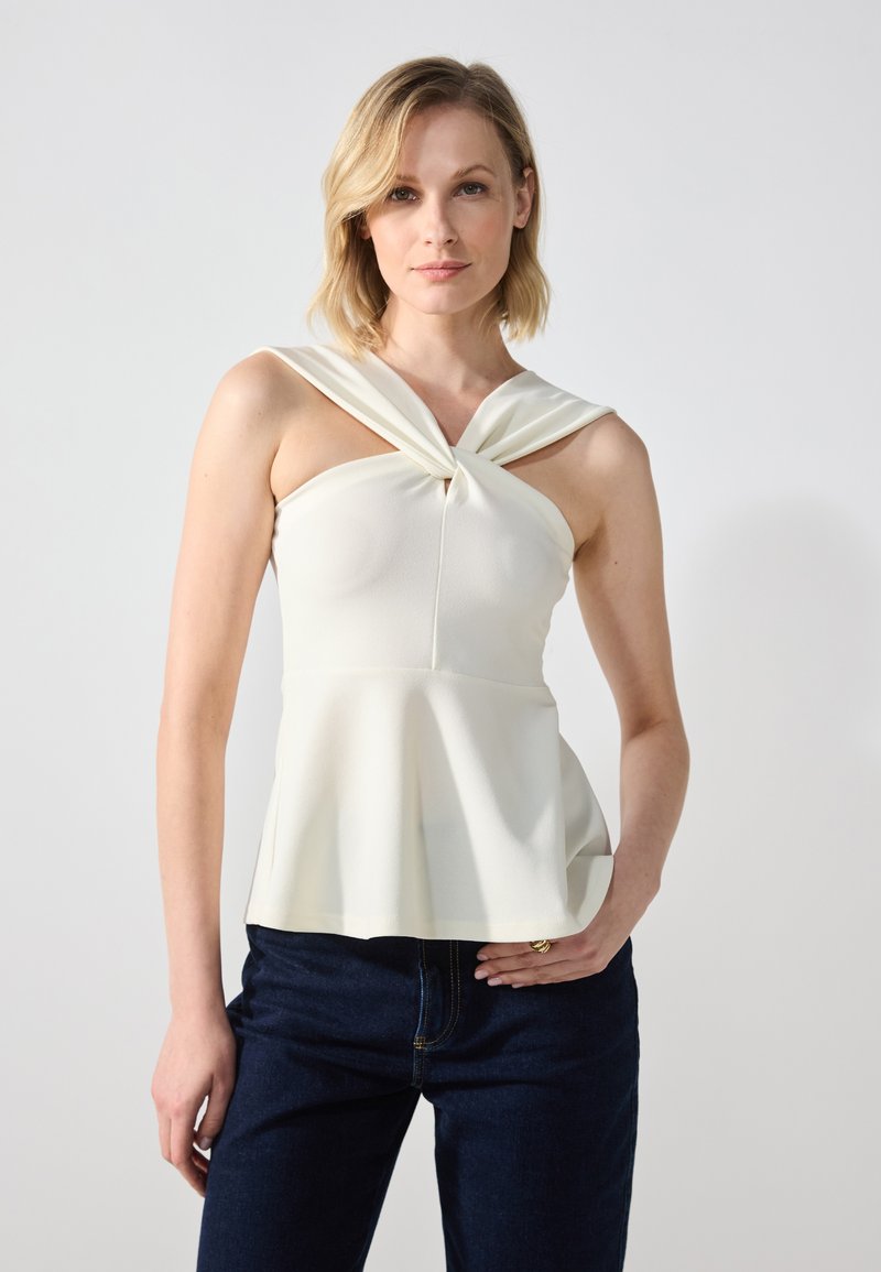 Off-white peplum-topp i lett stoff med en knyttet, drapert utringning. Kombinert med mørkeblå jeans som fremhever en tettsittende look.
