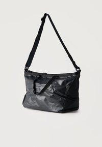 Μεγάλη μαύρη τσάντα ώμου με ρυθμιζόμενο ιμάντα και δύο μικρές λαβές, κατασκευασμένη από γυαλιστερό, ελαφρώς ζαρωμένο υλικό, εμφανιζόμενη σε λευκό φόντο.