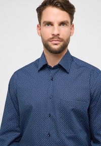 Camicia color blu navy con motivo a griglia di piccoli puntini bianchi e blu, colletto con bottoni e maniche lunghe con dettaglio tasca.