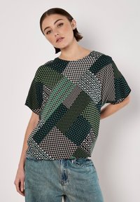 Kurzarmoberteil mit einem geometrischen Patchwork-Design in Grün, Schwarz und Weiß. Leichter Stoff mit unterschiedlichen Mustern und Rundhalsausschnitt.