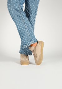 Beige sneakers with textured fabric and suede accents, paired with light blue denim flared pants featuring a raised pattern and frayed hem.