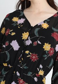 Czarna sukienka w kwiaty z dekoltem w kształcie litery V, z zapięciem na guziki oraz kolorowymi motywami kwiatowymi w odcieniach czerwieni, żółci i purpury na ciemnym tle.